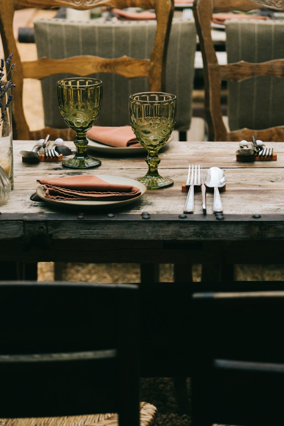 Rustic wooden table set with plates, napkins, and green goblets.